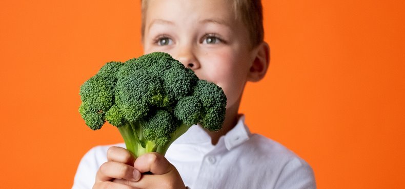 Dečak drži brokoli ispred narandžaste pozadine